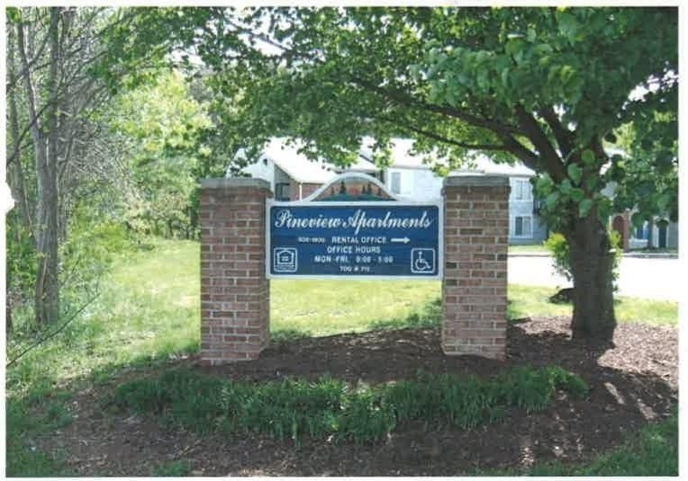 The Pineview Apartments entrance sign on brick pillars, with buildings and trees behind